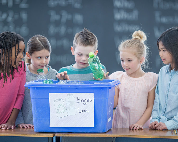 Five young kids put water bottles into a container.