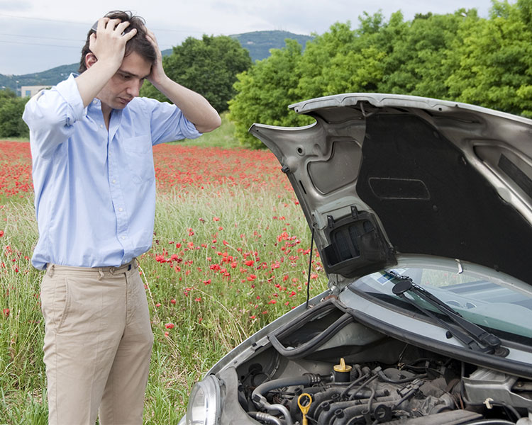 A man holds his hands to his head as he looks at his car’s engine.