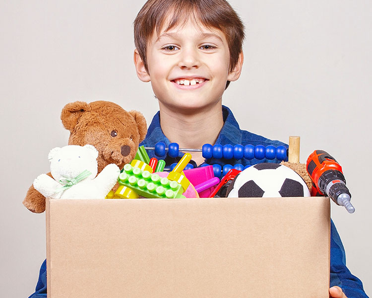 A young boy smiles while holding a box full of toys.