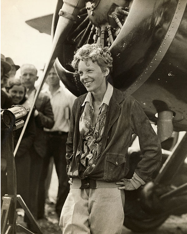 Amelia Earhart smiles next to her plane’s propeller.