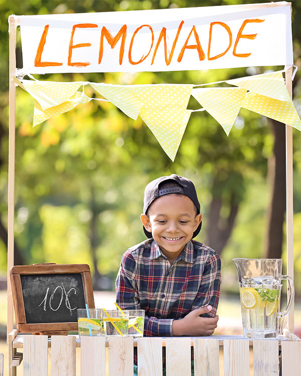 A kid smiles at a lemonade stand.