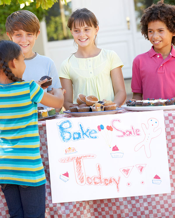 Three kids sell cupcakes at a bake sale.