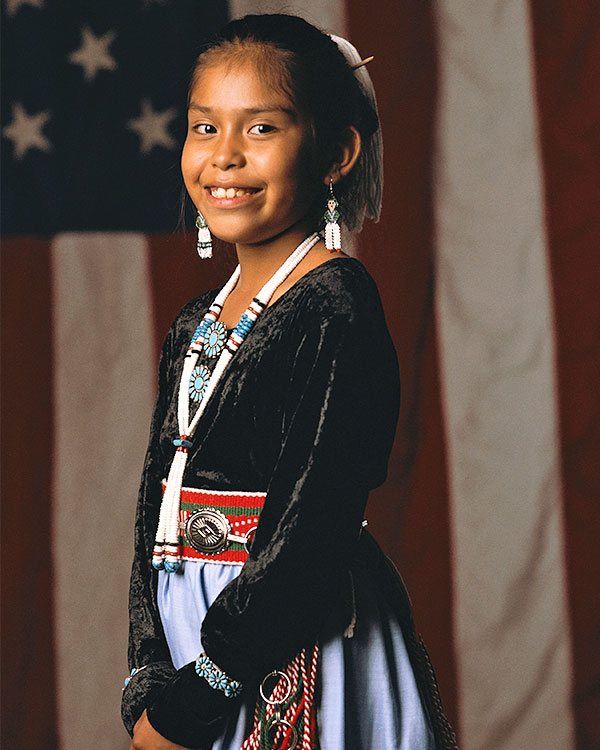 A young girl smiles while dressed in traditional regalia