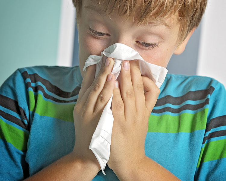 A young boy blows his nose into a tissue.