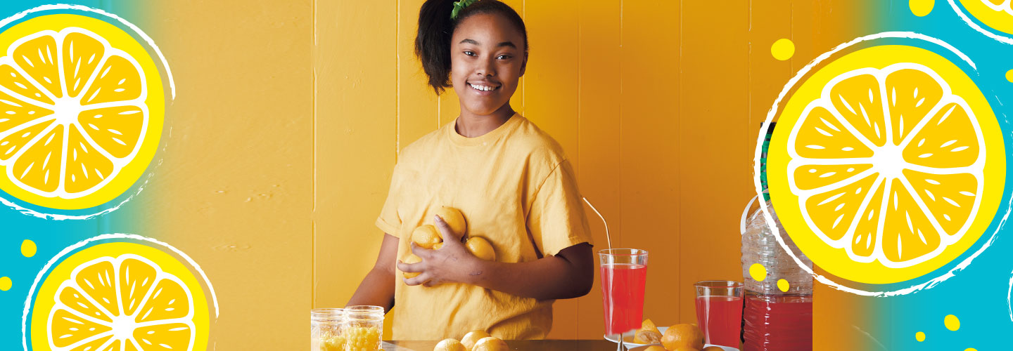 Girl holding lemons standing at a lemonade stand
