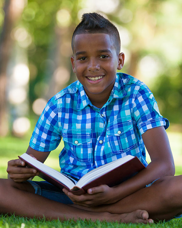 A young boy smiles and sits while reading a book