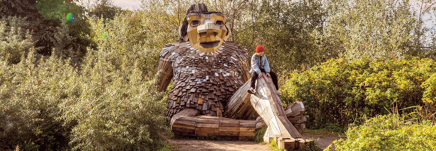 A man sits on the knee of a large wooden troll sculpture