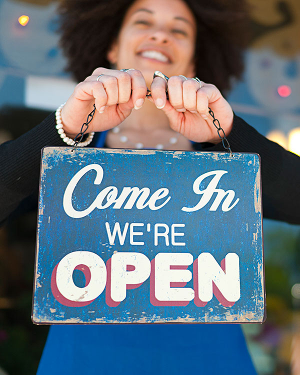 A woman holds a sign that says come in we’re open