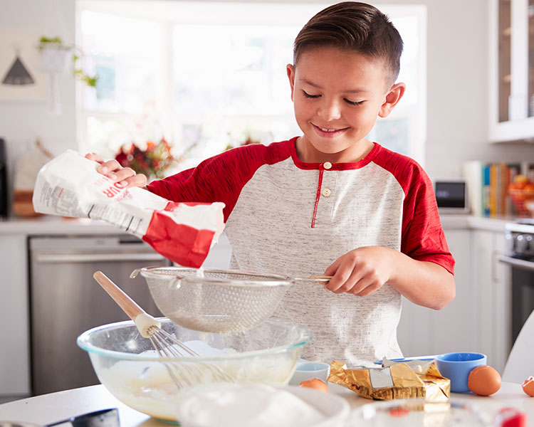 boy in kitchen sifting flour with baking ingredients around him