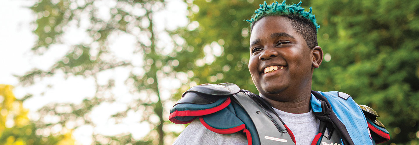 A smiling boy with blue small twisted hair wearing football gear