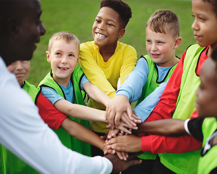 Children standing in a circle with their hands on each other&apos;s as they smile at an adult