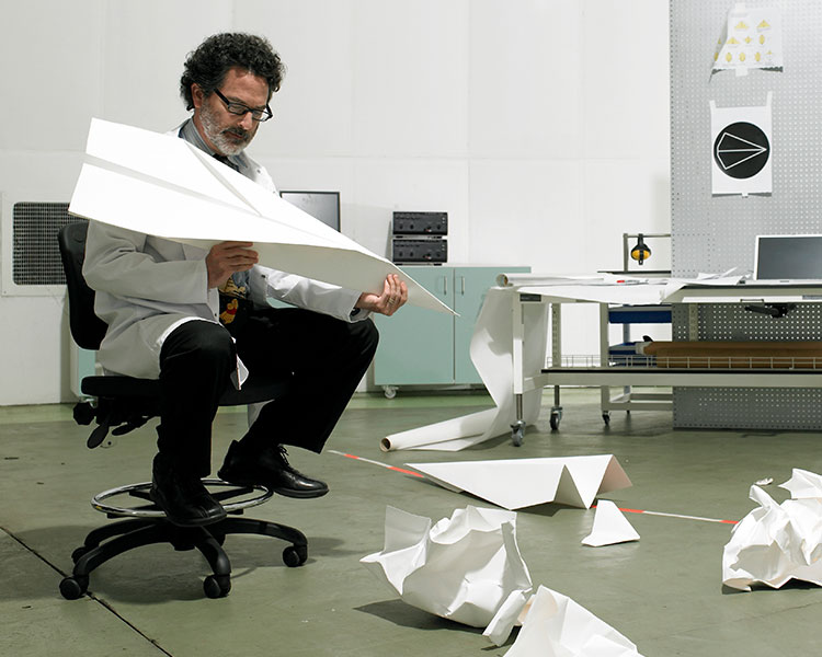 Image of a person making a giant paper airplane and other versions of it on the floor