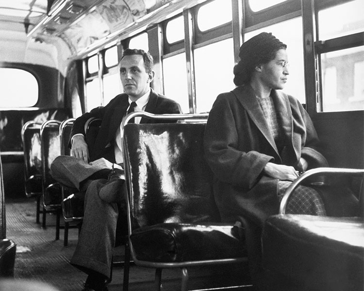 Black & white photo of Rosa Parks sitting on a bus with a white person sitting behind her