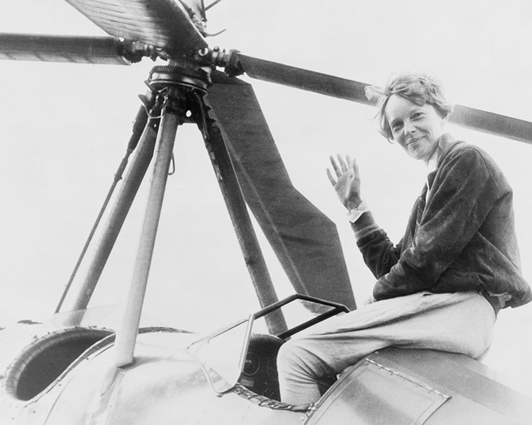 Black & white photo of Amelia Earhart smiling & posing on top of a plane