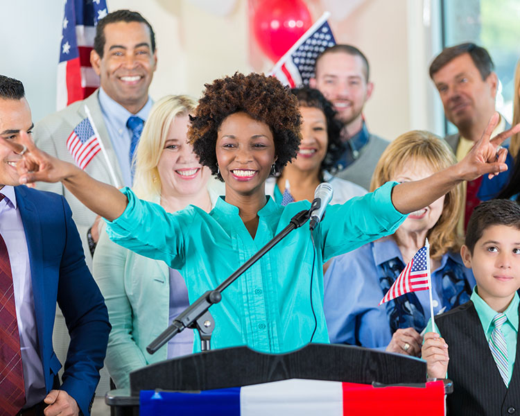 Photo of a political candidate at the podium with their supporters in background