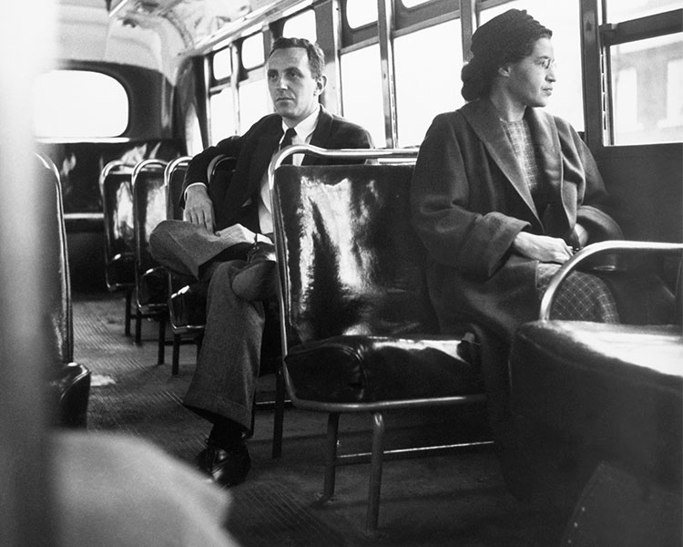 Black & white photo of Rosa Parks sitting on a bus while a white man sits behind her