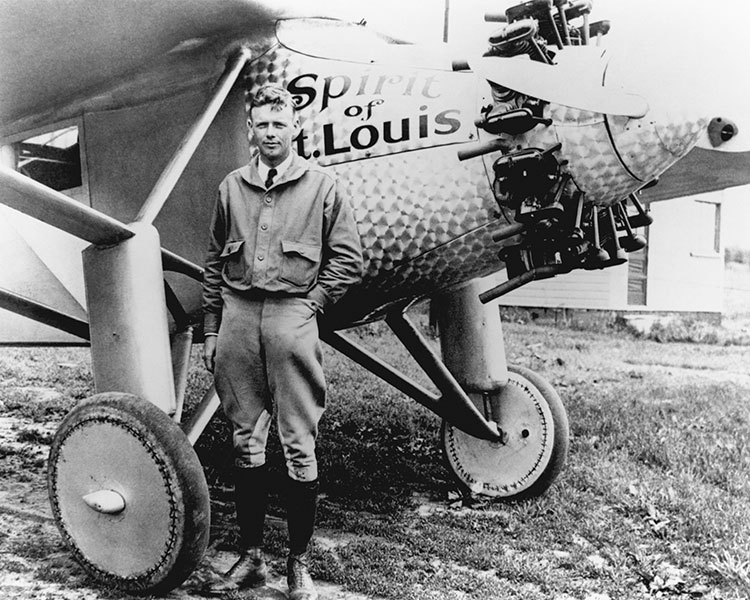 Black & white photo of a pilot posing by their small plane