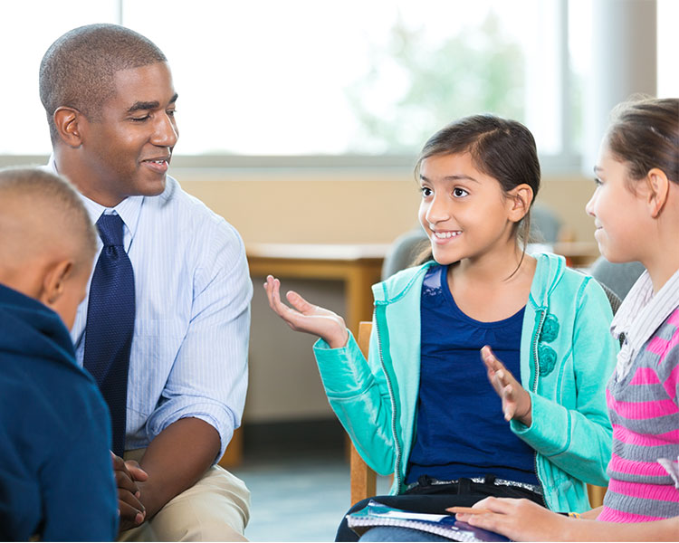 Image of students having a conversation with a teacher while sitting in a group