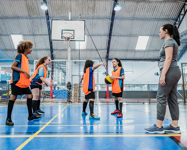 Photo of kids playing basketball with coach watching