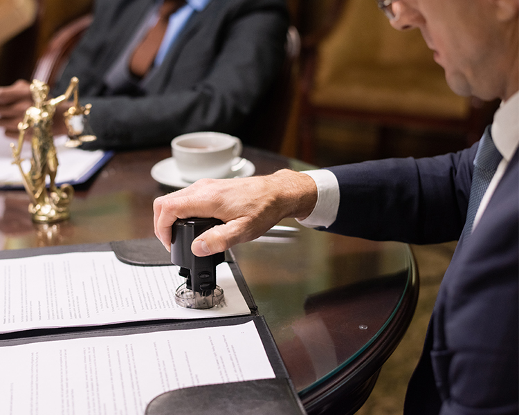 A person wearing a suit pressing a stamp into a document